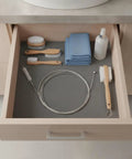 Heavy Duty Flexible Steel Drain Auger Knocks Stubborn Sink Clogs Dead alongside cleaning brushes and towels in a bathroom drawer.