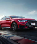 A sleek red sedan driving on a highway, showcasing a prominent front grille and dynamic silhouette under a clear blue sky.