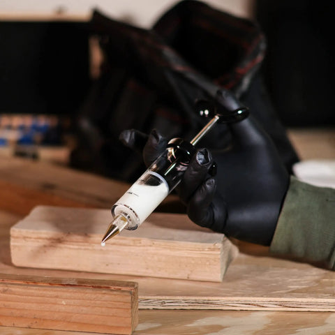 Slick Precision Wood Glue Syringe With Replaceable Tips for Tight Joints and Crafts held over wood pieces.