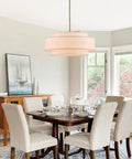 Totally Iconic 24 Inch Linen Drum Chandelier With Six Warm Lights Featuring Sleek Gold Frame And Three Tier Vintage Farmhouse Design illuminating a modern dining room.