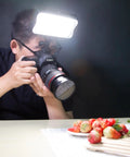 Person using Bi-Color LED Video Light 3300K-5600K With Dimmable Brightness For DSLR And Camcorder in a dark setting