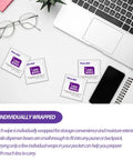 Lens wipes packets, five individually wrapped, on a white desk with laptop and eyeglasses.