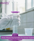 Durable Pro Grade Borosilicate Glass Measuring Cylinder Set With Hex Base And Brush Includes 10 ML 25 ML 50 ML And 100 ML Cylinders Class B Lab Glassware For Chemistry Experiments And Education. White-gloved hand holding measuring cylinder in lab.