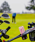 Pink outdoor portable Bluetooth boombox speaker waterproof, attached to a golf cart against a golf course background