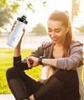 Woman holding On The Go 550ml Leak Proof Bike Water Bottle With Hands Free Bite Valve, outdoors in a park setting
