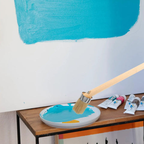 Wood Stain And Paint Brush With Wooden Handle 50mm Round Head for trim, furniture and wall finishes, placed on a table with blue paint.