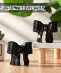 Black Coquette Bow Toilet Bolt Covers Set Of Two - Durable Ceramic Screw Nut Caps For Bathrooms displayed on a table.