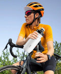 Cyclist holding an On The Go 550ml Leak Proof Bike Water Bottle With Hands Free Bite Valve, wearing cycling gear on a bike ride.