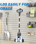 Cordless 9 Inch Mini Lawn Mower With 6000 RPM Brushless Power, folded for storage on a slat wall in a small yard area.