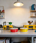 Compact Desktop Filament Extruder And Maker Machine For 3D Printers; yellow unit with spools of red, green, and yellow filament.