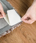 Applying non slip rug pad grippers for hardwood and tile under a grey area rug with fringes, showing double sided rug tape application.