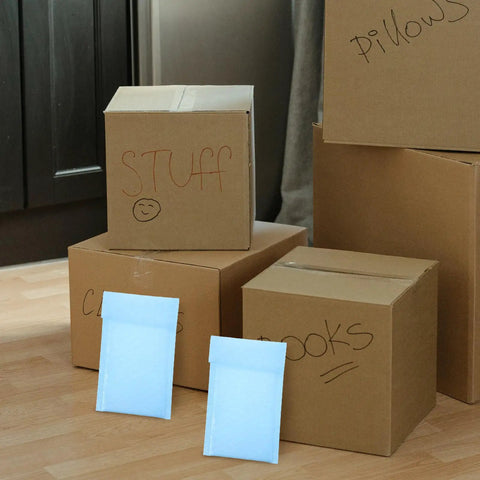 Milk Blue Bubble Mailer Bags 100 Pack Self Sealing 11x15 Plus 4 Inch with boxes labeled 'Stuff' and 'Pillows' in background