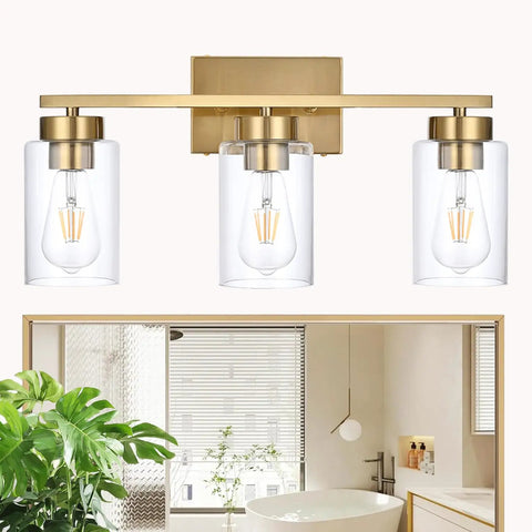 Clean Three Light Bathroom Vanity Wall Sconce In Smooth Brushed Gold Finish With Clear Retro Glass Shades over a modern bathroom mirror.