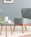 Stylish gray upholstered chair beside a round wooden table with a white kettle and cup, ideal for cozy living spaces.