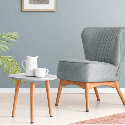 Stylish gray upholstered chair beside a round wooden table with a white kettle and cup, ideal for cozy living spaces.