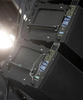 Stacked black audio speakers with handles and wiring, installed on stage lighting setup.