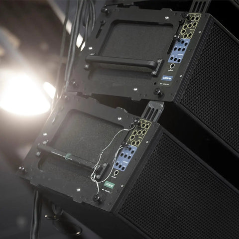 Stacked black audio speakers with handles and wiring, installed on stage lighting setup.