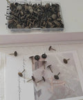 Top Shelf Antique Brass Daisy Upholstery Tacks And Slick Decorative Furniture Nails Pro Grade Pack Of 200 Pieces, showing decorative nails in a clear box.