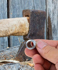 Hand holding iron wedge near axe handle, Heavy Duty Splitting Handle Metal Tapered Wedge For Axe Installation And Axe Handle Crafting.