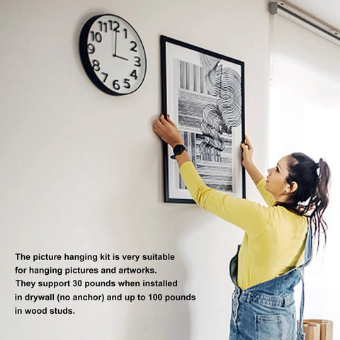 Woman hanging artwork with Heavy Duty Picture Hangers And Double Headed Wall Hooks With Bulletproof Grip Rating Up To 30 Lbs For Drywall Or Wood Studs Zero Hassle Setup Hang Gallery Walls Without Sweat Includes 30 Pack.