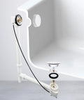 No Sweat Installation 27 Inch Cable Drive Bath Drain Trim Kit Featuring Top Shelf Brass Rotary Overflow Knob And Secure Pop Up Stopper For Stress Free Plumbing Fixes White exposed under bathtub.