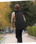 Person riding an electric scooter wearing a Flat Out Rugged Oxford Drum Pouch Waterproof Percussion Storage Case Built Boss Level For Studio Jams Gig Dates Weekend Campouts And Travel Hauls Black on their back.