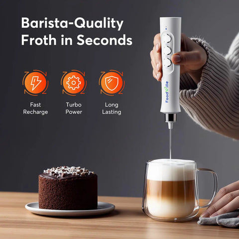 Person using Rechargeable Milk Frother Handheld Foam Maker With Stainless Whisk For Cappuccino Latte Bulletproof Coffee Keto Diet Protein Powder Matcha Pure White Two Whisks No Fuss Quick Froth to froth milk in clear glass mug beside a dessert.