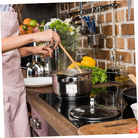 Person cooking with a stainless steel pot on a stovetop, surrounded by fresh vegetables and kitchen utensils.