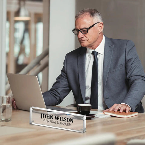 Man working at desk with 4 Pack Clear Acrylic Desk Name Plates Set With Double Sided Design, Personalized Office Name Tag Blocks visible.