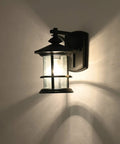 Illuminated massive 12.5 inch outdoor wall light fixture with textured black finish and clear seeded glass shade, E26 base.