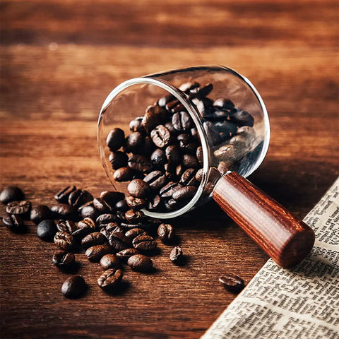 Single Spout Espresso Shot Glass With Wood Handle filled with coffee beans on a wooden table, showcasing borosilicate glass detail.