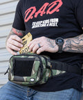 Person holding an emergency diaper kit with a camo waist pack, wearing a D.A.D. shirt, highlighting on-the-go parent convenience.