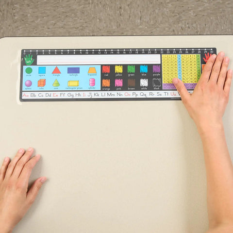 EZ-Fit Desktop Helper Tape Strips Pack of 36 Student Desk Name Tags applied on a desk with a ruler and colorful shapes visible