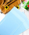 Milk Blue Bubble Mailers 11x15 Plus 4 Inch Self Seal Padded Envelopes on white wooden table near brown bag and floral cup