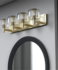Vintage Brushed Brass Vanity Light with Clear Glass Globe Lampshades, 29 Inch 4 Light Bathroom Fixture on wall above mirror.