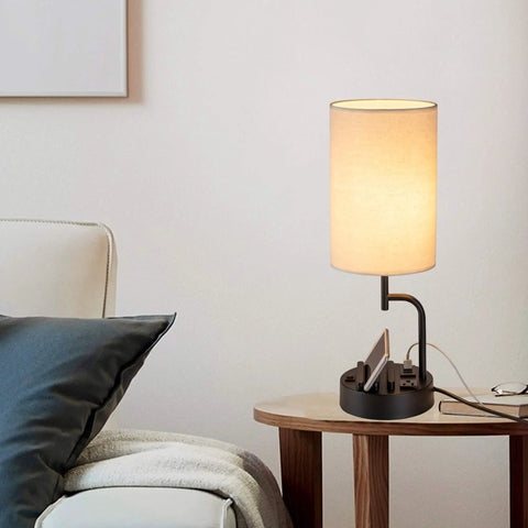 Cream bedside table lamp with three USB ports and AC outlet, phone stands, in modern living room, charging hub visible.