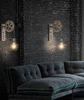 Industrial Pulley Wall Sconce With Matte Iron Cage And Wood Wheel Bronze Color Vintage Mid Century Revival Indoor Lighting For Barn Restaurant Farmhouse Industrial Chic Vibe in living room setting with dark sofa and brick wall.