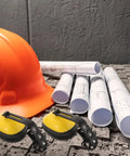 Heavy Duty Yellow Hard Hat Mount Ear Muffs With Tough As Nails Adjustable Fit And Powerful Noise Reduction For Daily Grind Worksite Safety And Pro Level Hearing Protection beside an orange hard hat and blueprint rolls.