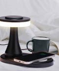 Rechargeable LED Table Lamp With Wireless Charging Pad Dimmable Night Light For Bedroom Patio Nursery Or Restaurant Ambience Cozy Vibes Portable USB Cable Included Black with phone charging and mug nearby