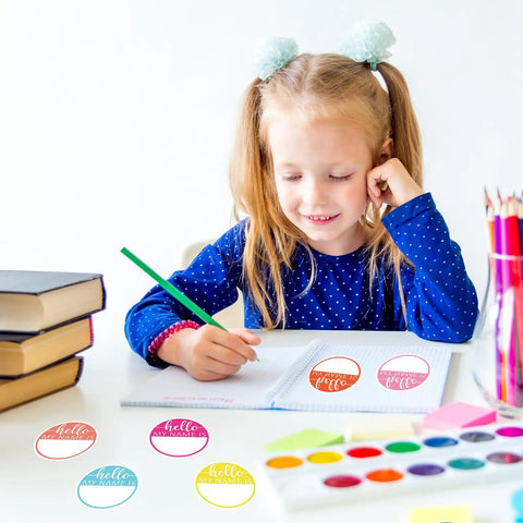 Child using Hello My Name Is Round Name Tag Stickers Set 315 Pcs In 9 Macaron Colors for classroom activity at desk.