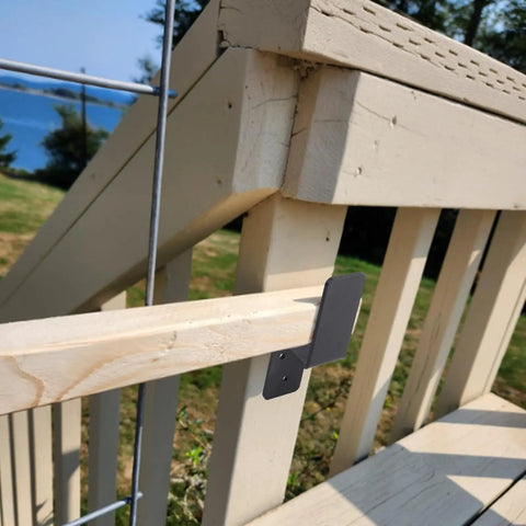 Side view of heavy-duty door barricade bracket installed, holding a 2x4 board for home security on outdoor wooden stairs.