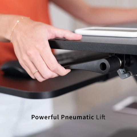 Person adjusting No Brainer Height Adjustable 25 Inch Standing Desk Converter for sit and stand setup with gas spring lift.