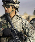 Two soldiers in camouflage uniforms with tactical gear and helmets, one holding a rifle in a desert setting.