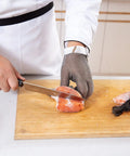 Person using a knife to slice salmon while wearing a Chainmail Glove Cut Resistant Food Grade Stainless Steel Mesh Safety Glove For Butchers Oyster Shucking Mandoline Slicing Fish Fillet Medium Size Ultra Flexible 304 Stainless Rings For Superior Hand Protection.