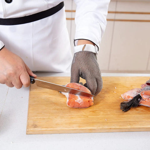 Person using a knife to slice salmon while wearing a Chainmail Glove Cut Resistant Food Grade Stainless Steel Mesh Safety Glove For Butchers Oyster Shucking Mandoline Slicing Fish Fillet Medium Size Ultra Flexible 304 Stainless Rings For Superior Hand Protection.