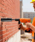 Cordless orange drill with black diamond core bit attached drilling into a red brick wall; worker wearing safety vest.