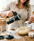 Electric Hand Mixer And Immersion Blender With Six Attachments Including Wire Whisk Milk Frother And Food Chopper Heavy Duty Handheld Kitchen Tool mixing batter in a glass bowl