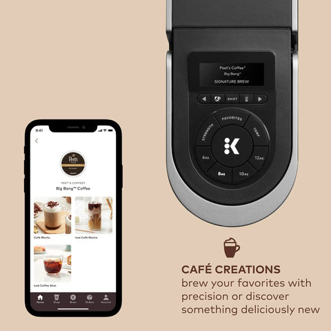 Top view of Smart WiFi Single Serve Coffee Maker For Home Baristas That Delivers Coffee Lattes And Cappuccinos With Built In Frother BrewID Pod Recognition And Six Brew Sizes Black next to a smartphone displaying the coffee maker app.