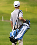 Child carrying X7 Junior Kids Golf Set Right Handed With Driver Hybrid Irons Putter Stand Bag on a golf course.