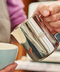 32 Oz Milk Frother Pitcher With Clear Scale, 304 Stainless Steel Steaming Jug And Latte Art Pen in hand next to cup